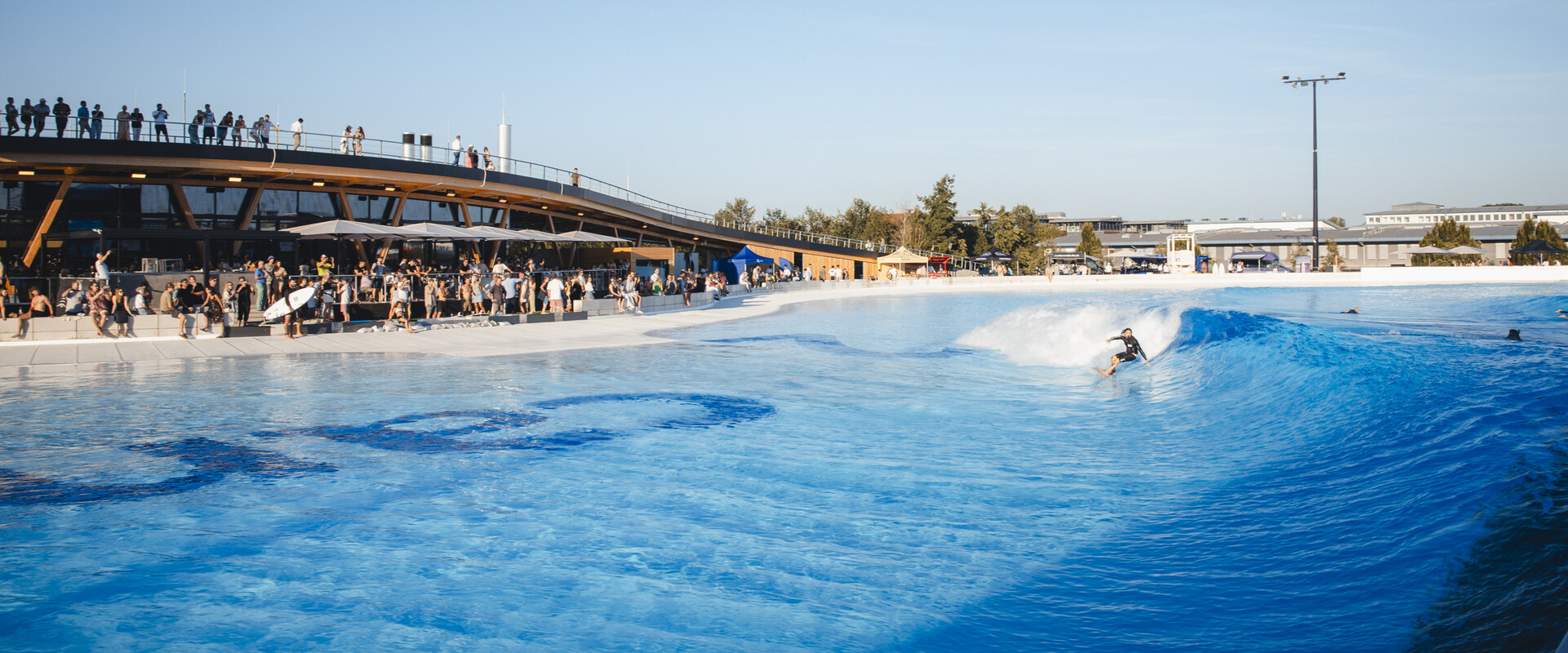 Surfer:innen im Wavepool des Surfparks bei M&uuml;nchen, die gemeinsam perfekte Wellen reiten &ndash; Surfen f&uuml;r alle Levels.