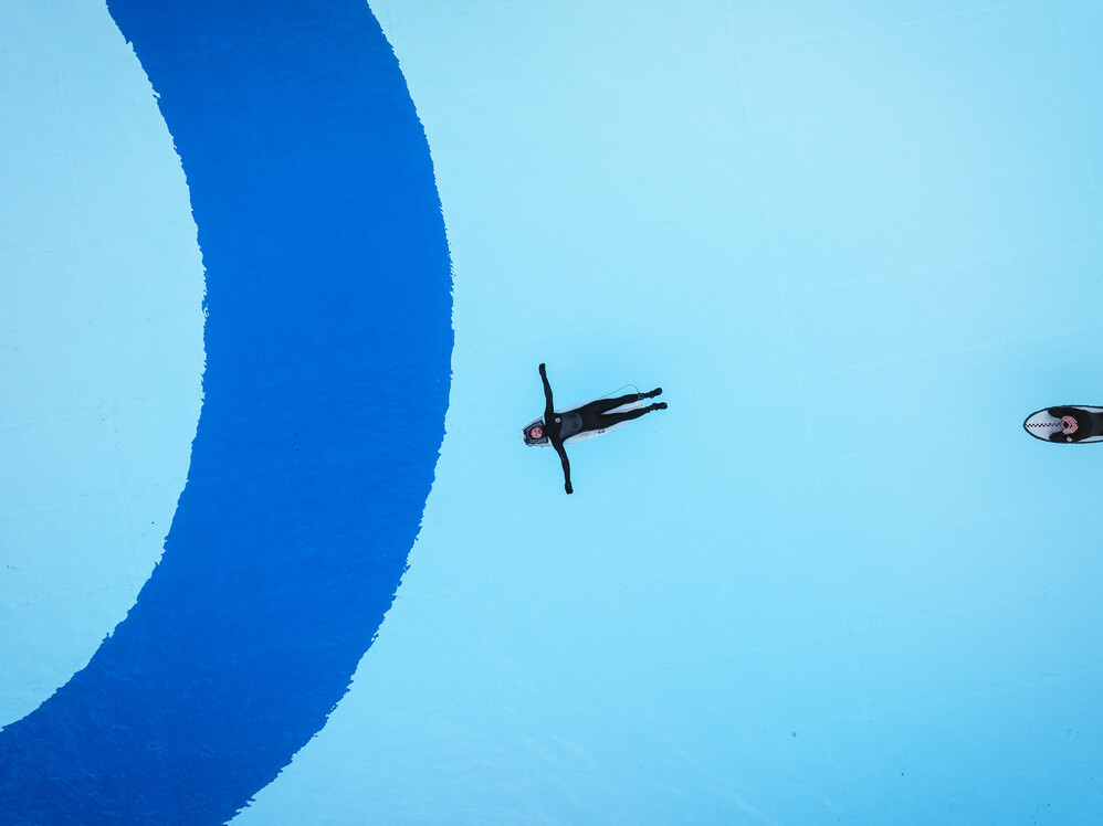 Die Surftown soll ein freizug&auml;nglicher Ort f&uuml;r alle sein, an dem man sich treiben lassen und sportlich austoben kann. Das Bild zeigt einen Surfer aus der senkrechten Draufsicht, der r&uuml;cklings auf seinem Board liegt, die Arme seitlich von sich gestreckt und auf seinem Board im ruhigen Wasser floatet.